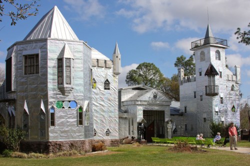 A whimsical castle made of shiny materials, featuring towers and unique architectural details, set in a grassy area.