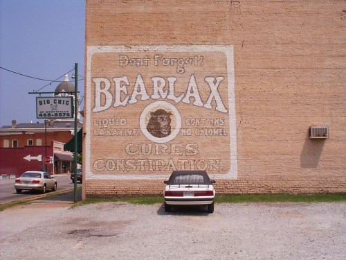 Faded mural on a brick wall advertising Bearlax, a liquid laxative, with a parked car in front.