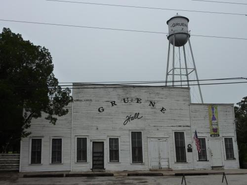 Historic Gruene Hall building with a water tower in the background, surrounded by trees and power lines.