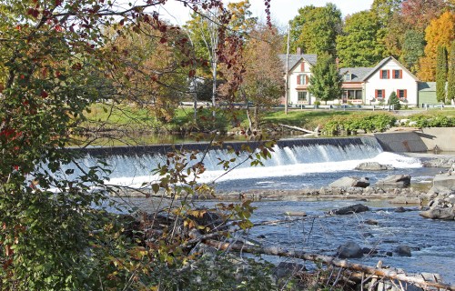 A serene scene featuring a waterfall, a river, and a charming house surrounded by autumn foliage.