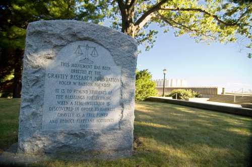 A stone monument with an inscription about the Gravity Research Foundation, surrounded by trees and a park-like setting.