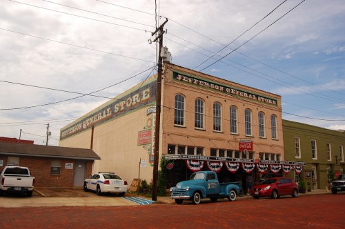 Historic Jefferson General Store with patriotic decorations, vintage cars parked, and a cloudy sky in the background.