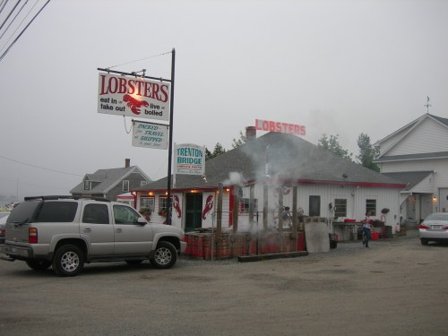 A seafood restaurant named "Lobsters" with a sign, smoke rising, and a parked SUV in a foggy setting.