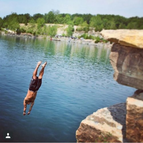 A person diving into a clear blue lake from a rocky ledge on a sunny day.