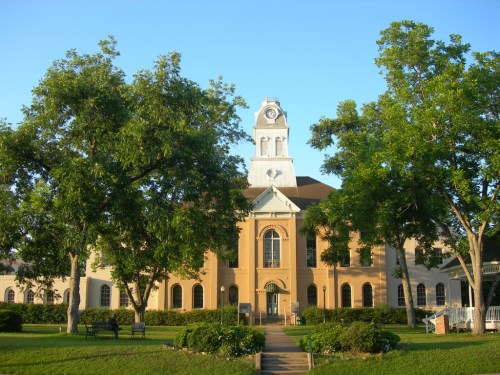 Historic building with a clock tower, surrounded by green trees and a clear blue sky.