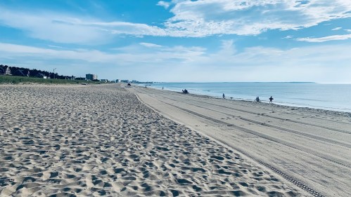A sandy beach stretches along the shoreline under a blue sky, with a few people walking in the distance.