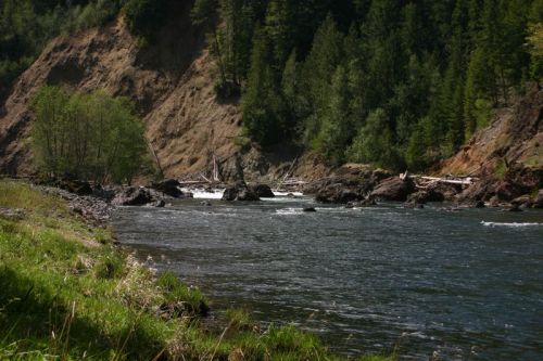 A serene river flows through a lush green landscape, surrounded by rocky cliffs and trees.