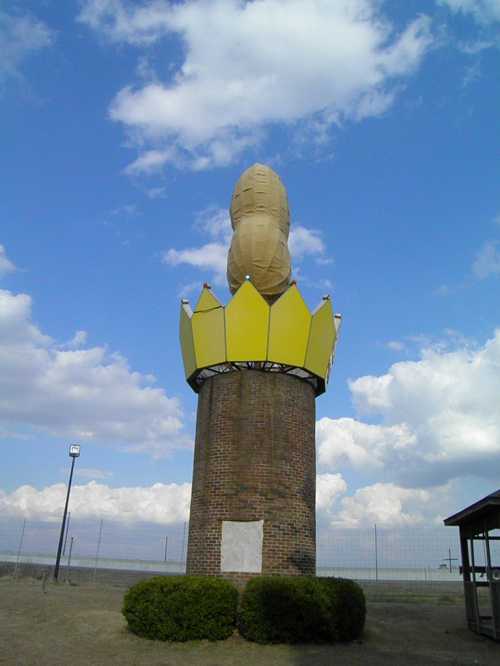 A tall, whimsical structure resembling a peanut atop a yellow crown, set against a blue sky with fluffy clouds.