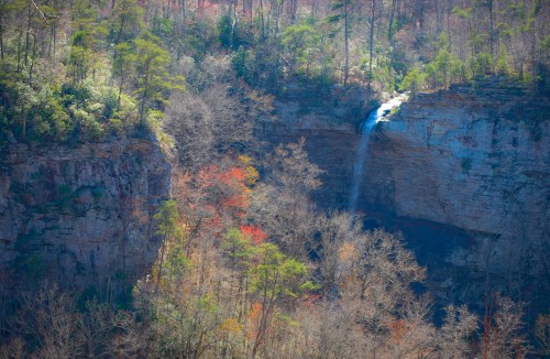 A scenic view of a waterfall cascading down a rocky cliff, surrounded by trees with autumn foliage.