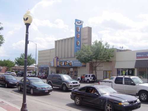 A street view of a UFO museum with cars parked outside and a lamppost in the foreground under a cloudy sky.