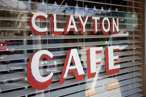 Sign for "Clayton Cafe" displayed on a window with blinds partially closed.