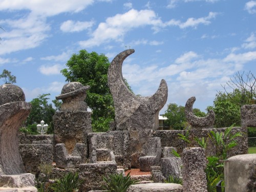 Stone sculptures resembling celestial bodies under a blue sky with scattered clouds and greenery in the background.