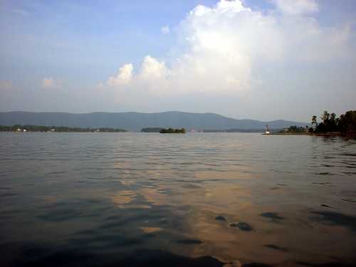 A serene lake scene with calm waters, distant mountains, and a few clouds in a blue sky.