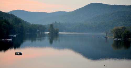 Serene lake surrounded by misty mountains at dawn, with boats gently floating on the calm water.