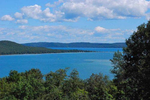 A serene lake surrounded by green hills and blue skies with fluffy clouds, reflecting a peaceful natural landscape.