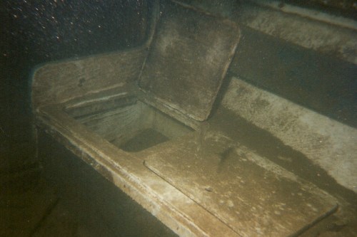 An old, weathered wooden box with a lid, submerged underwater, surrounded by sediment and debris.