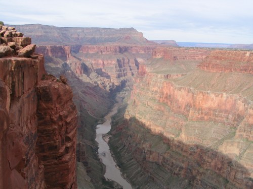 A panoramic view of the Grand Canyon, showcasing steep red rock formations and a winding river below.