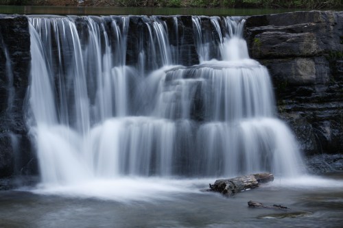 A serene waterfall cascading over rocks, creating a misty effect in a tranquil natural setting.