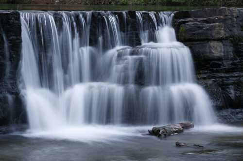 A serene waterfall cascades over rocky ledges, creating a smooth flow of water into a calm pool below.