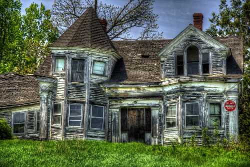 An old, weathered house with a turret, overgrown grass, and a "Do Not Enter" sign.