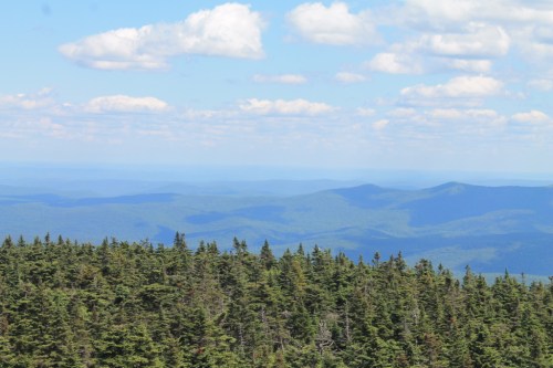 A panoramic view of rolling green mountains under a blue sky with fluffy white clouds.