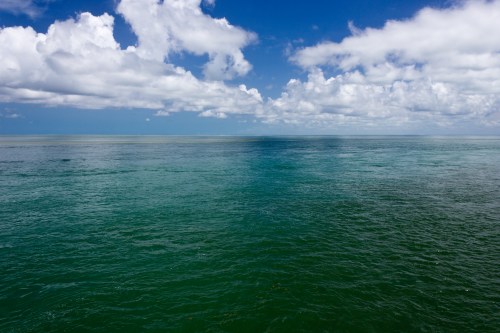 A serene ocean view with calm turquoise waters and a bright blue sky dotted with fluffy white clouds.