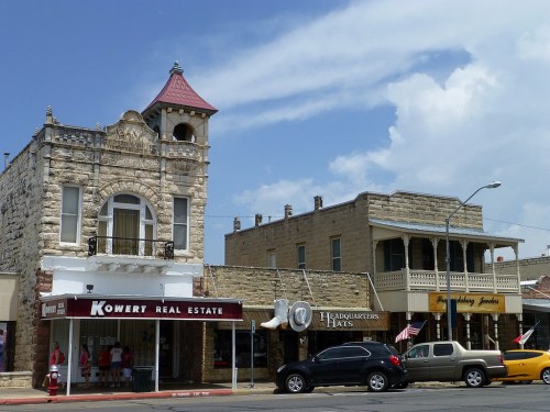 Historic buildings with unique architecture, featuring a tower and storefronts, under a blue sky with clouds.