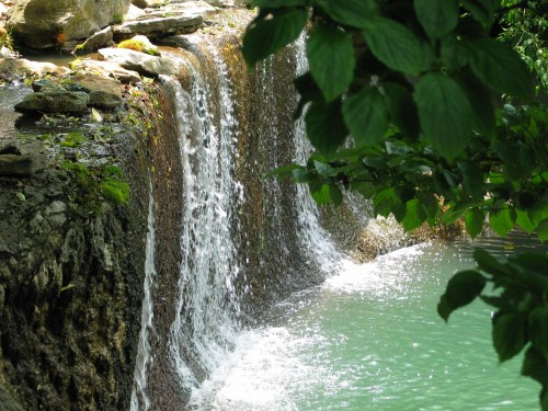 A serene waterfall cascading over rocks into a tranquil turquoise pool, surrounded by lush green foliage.
