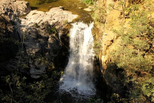 A serene waterfall cascading over rocky terrain, surrounded by lush greenery and a calm pool below.