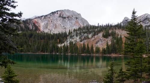 A serene lake surrounded by evergreen trees and rocky mountains, reflecting the landscape in calm waters.