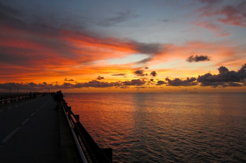 A vibrant sunset over calm waters, with colorful clouds reflecting in the sky and a pier in the foreground.