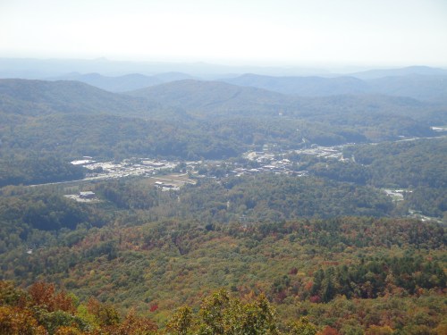 A panoramic view of a valley surrounded by mountains, showcasing a small town nestled among colorful autumn foliage.