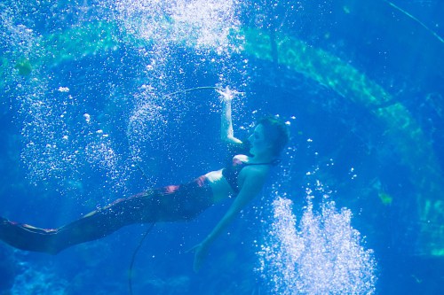 A mermaid swims gracefully underwater, surrounded by bubbles and vibrant blue water.