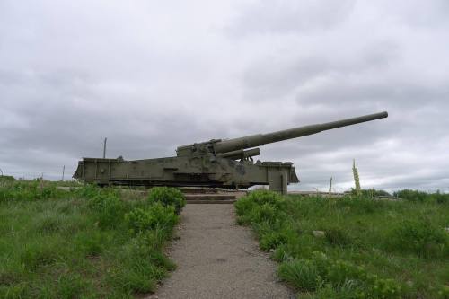 A large military artillery piece on a grassy landscape under a cloudy sky.