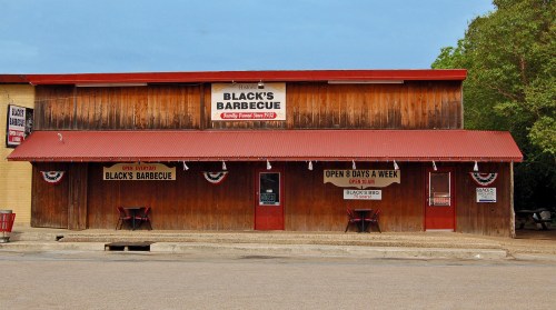 A rustic barbecue restaurant with a wooden exterior, featuring signs and patriotic decorations.
