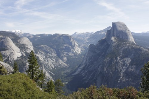 A panoramic view of a mountainous landscape with rocky peaks and lush green valleys under a clear blue sky.