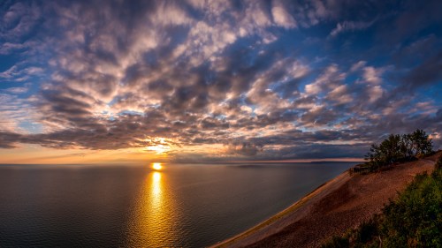 A panoramic view of a sunset over a calm lake, with dramatic clouds reflecting warm colors in the sky.