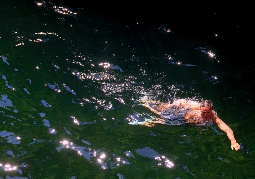 A person swims in clear, sparkling water, surrounded by dark shadows and reflections of light.