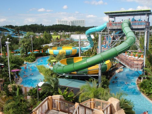 A vibrant water park featuring colorful slides, lazy rivers, and lush greenery, with visitors enjoying the attractions.