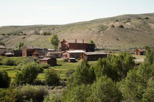 A scenic view of a historic village with wooden buildings surrounded by greenery and rolling hills in the background.
