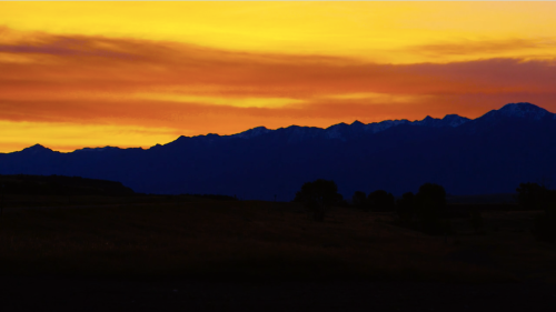 Silhouette of mountains against a vibrant orange and yellow sunset sky.