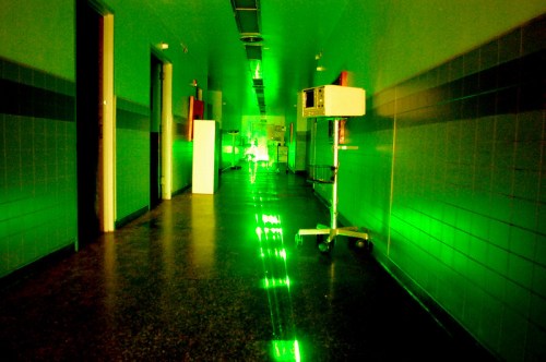 A dimly lit hospital corridor with green lighting and medical equipment on wheels.