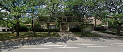 A large, two-story house surrounded by trees, with a stone pathway and a well-maintained lawn in front.