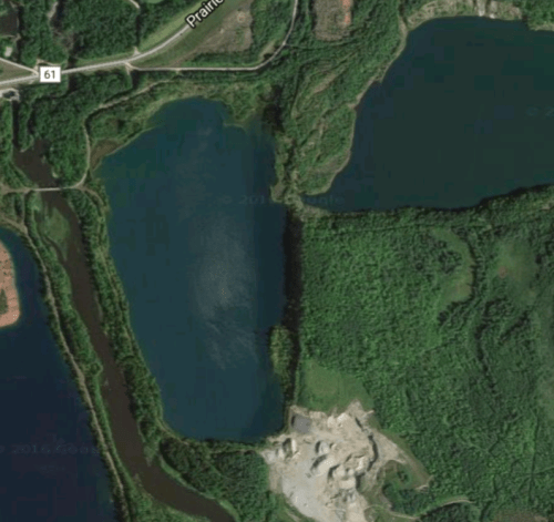 Aerial view of a forested area with two lakes and a gravel pit in the foreground, surrounded by greenery.