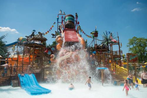 A vibrant water park with a large slide, kids playing in the water, and colorful structures under a clear blue sky.