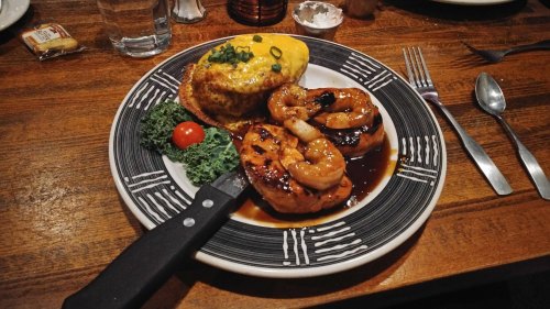 A plate of grilled shrimp and chicken with a side of omelette, garnished with greens and a cherry tomato.