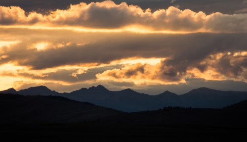 Dramatic sunset over mountain silhouettes, with vibrant clouds and golden light illuminating the sky.