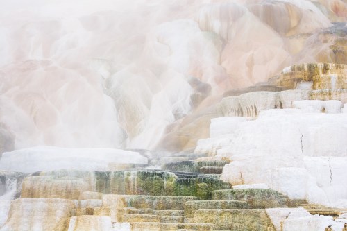 A misty landscape of colorful mineral terraces, showcasing layers of white, yellow, and green formations.