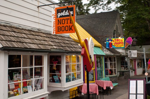 Colorful storefronts of shops, including a bookstore and a Mexican restaurant, with outdoor seating and signage.