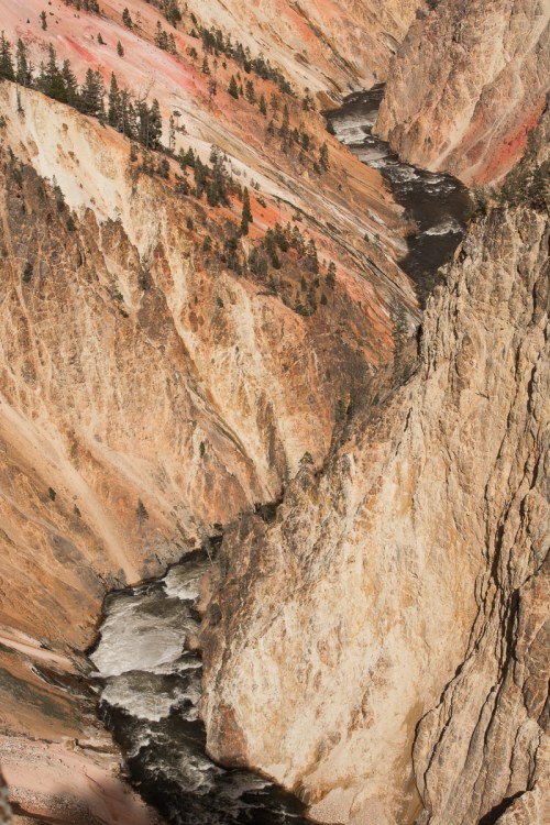 A winding river flows through a colorful canyon with steep, rocky cliffs and scattered trees.